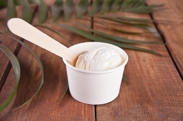 Helado de vainilla con cuchara y hoja de palma en mesa