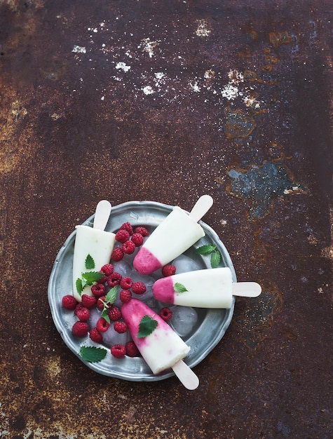 Helado de yogur de lima y frambuesa o paletas heladas con bayas frescas y cubitos de hielo en una placa de plata vintage sobre una vista superior de fondo de metal grunge