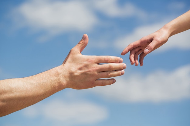 Helfen. Hände von Mann und Frau auf blauem Himmel