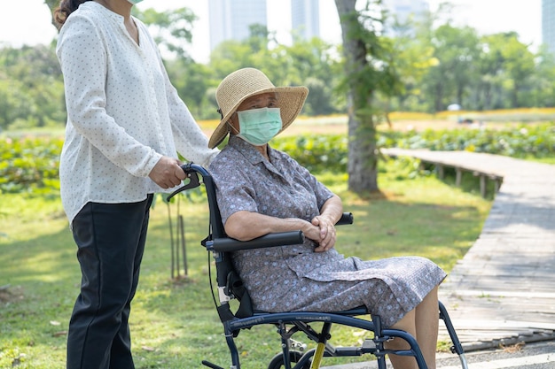 Helfen Sie asiatischen Senioren oder älteren alten Damen im Rollstuhl und tragen Sie eine Gesichtsmaske zum Schutz der Sicherheitsinfektion Covid19 Coronavirus im Park