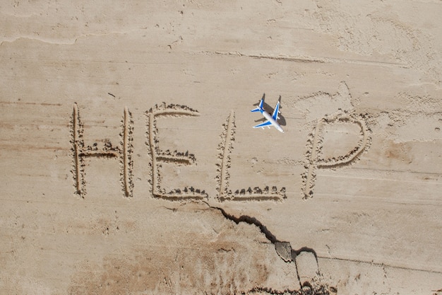 Helfen Sie mir die Inschrift und fliegen Sie auf den Sand Bitte helfen Sie mir an einem tropischen Strand