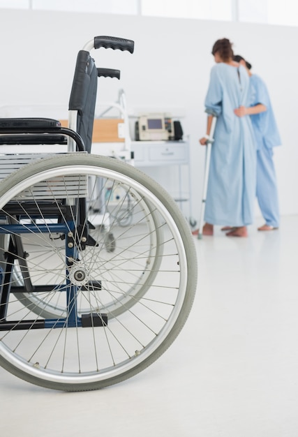 Helfender Patient Doktors, zum mit Rollstuhl im Vordergrund zu gehen