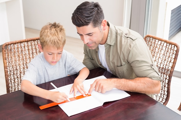 Helfender Sohn des hübschen Vaters mit Hausarbeit bei Tisch