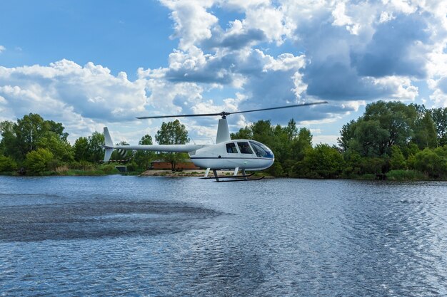Helicóptero branco sobre a água contra o céu e as árvores. Helicóptero sobre a água.