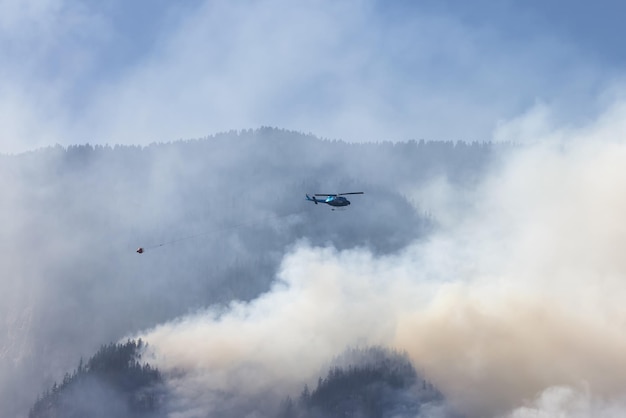 Helicóptero do serviço de incêndios florestais voando sobre incêndios florestais de BC e fumaça na montanha perto de Hope