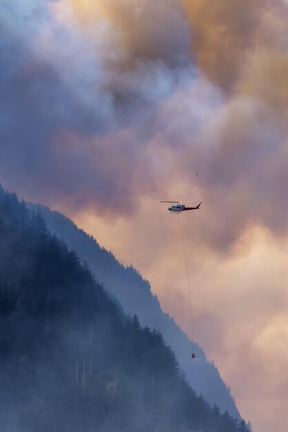 Helicóptero do serviço de incêndios florestais voando sobre incêndios florestais de BC e fumaça na montanha perto de Hope