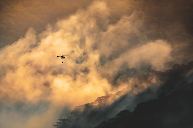 Helicóptero de extinción de incendios llevar balde de agua para extinguir el incendio forestal