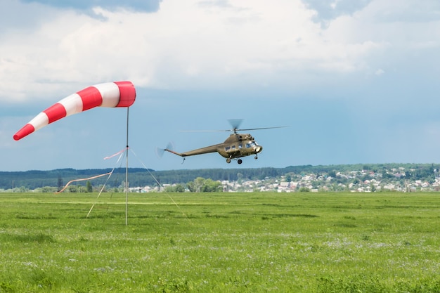 Helicóptero militar verde vuela cerca del suelo junto a una veleta contra el fondo de la ciudad