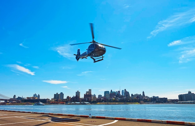 Helicóptero negro despegando del helipuerto en el Bajo Manhattan en Nueva York, EE.UU., en East River. Muelle 6. East River y rascacielos de Brooklyn al fondo