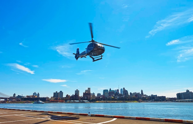 Helicóptero preto decolando do heliporto em Lower Manhattan, em Nova York, EUA, no East River. Pier 6. East River e arranha-céus do Brooklyn ao fundo