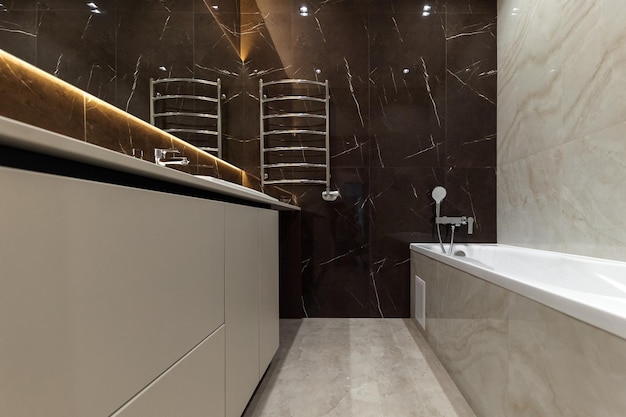 Hellbeiges und braunes modernes badezimmer mit badewanne und dusche und weißem schrank mit spiegel