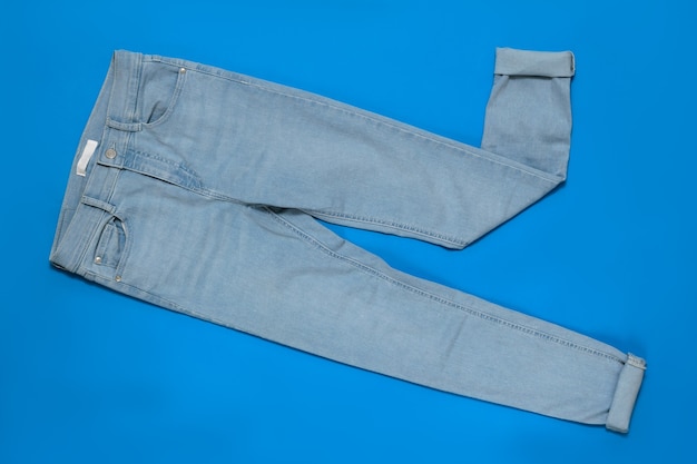 Hellblaue Frauenjeans mit Manschetten auf blauem Hintergrund. Das Konzept der modernen Mode für elektronische Geräte. Flach liegen. Der Blick von oben.