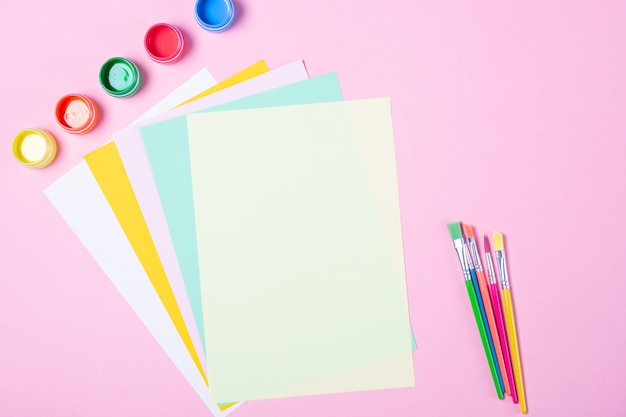 Helle Aquarelle, Pinsel, leeres farbiges Papier auf rosa Hintergrund. Freiraum. Die Schule beginnt mit dem Kunstkonzept