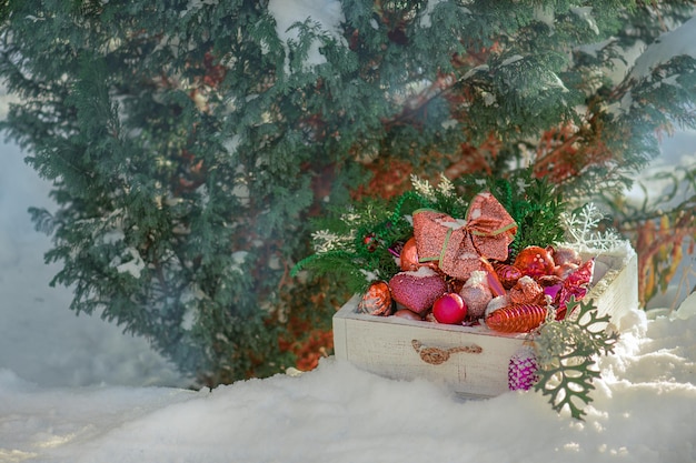 Helle Dekorationen in der Schachtel neben dem Weihnachtsbaum im Schneegarten
