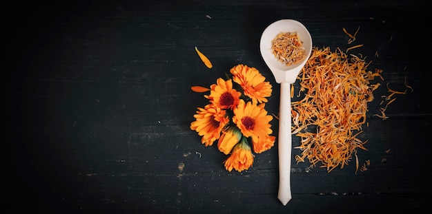 Helle frische Blumen und getrocknete Calendulablumen auf einem schwarzen hölzernen Hintergrund Draufsicht mit einer Kopie des Raumes.