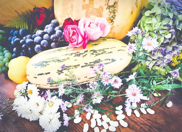 Helle Herbstkomposition aus Gemüse, Obst und Blumen. Melonen in verschiedenen Größen, Quitten, Trauben, Wildblumen, Rosen auf einem Holztisch. Ansicht von oben, Nahaufnahme.