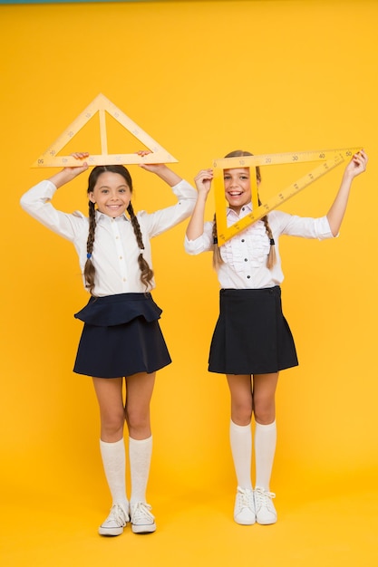 helle Köpfe. Kinder in Uniform an der gelben Wand. Freundschaft und Schwesternschaft. glückliche kleine mädchen studieren mathematik. Die Schüler verwenden das Gon-Lineal. Stamm Disziplinen. zurück zur Schule. Mathematik und Geometrie.