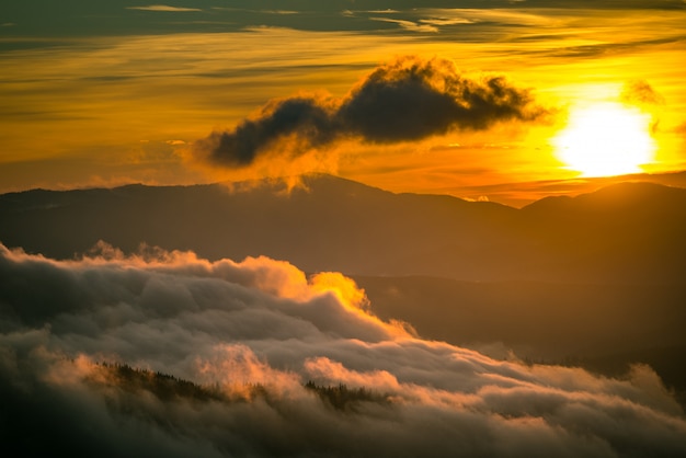 Helle Sonne, die hinter Bergen mit dramatischem Himmel auf Hintergrund untergeht