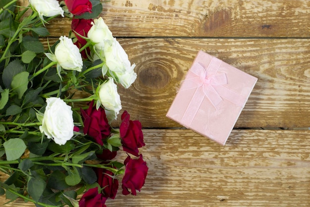 Helle weinrote und farbige Blumenrosen und rosa Geschenkbox in einem Blumenstrauß auf hölzerner Hintergrundnahaufnahme