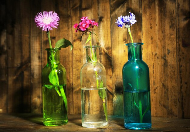 Helle Wildblumen in Flaschen auf Holzhintergrund