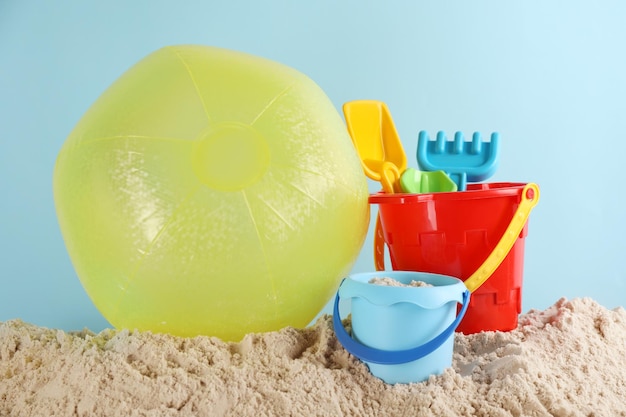 Heller aufblasbarer Ball und Strandspielzeug aus Kunststoff auf Sand vor hellblauem Hintergrund