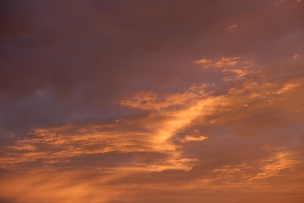 Heller, farbenfroher Sonnenuntergangshimmel mit lebendigen, glatten Wolken, die mit untergehendem Sonnenlicht beleuchtet werden, das sich bis zum Horizont ausbreitet