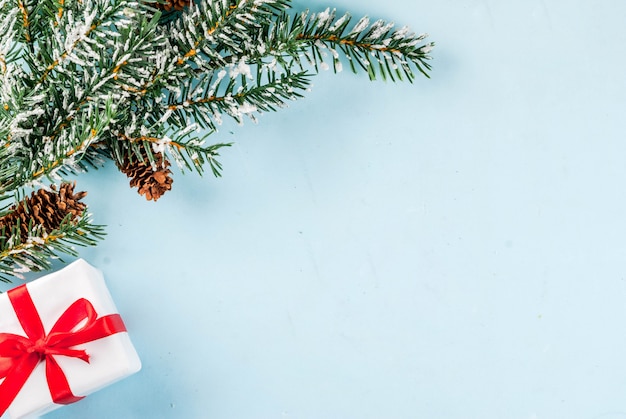 Heller Hintergrund des Weihnachten und des neuen Jahres, Grußkartenkonzept, Weihnachtsbaumaste mit Kiefernkegeln und künstlicher Schnee, mit Geschenkbox, Draufsichtkopienraum