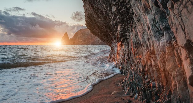 Heller Meeressonnenuntergang, die Wellen krachen in den Felsen, der vom warmen Sonnenuntergangssand und den vulkanischen Kieselsteinen beleuchtet wird