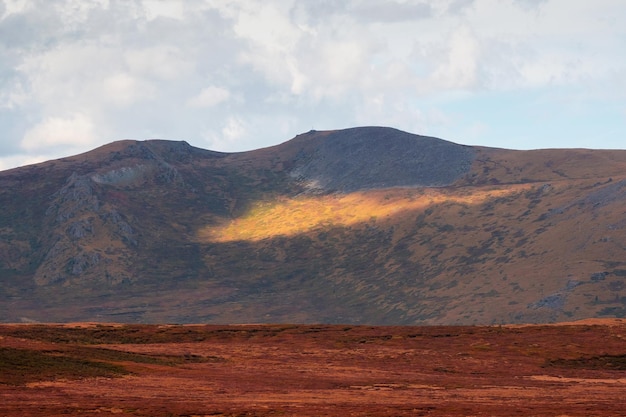 Heller schmaler Sonnenstrahl auf einem dunklen Berghang Stimmungsvolle Berglandschaft mit großen Felsen unter bewölktem Himmel Mystisches Licht in den nebligen dunklen Bergen Dramatischer Himmel auf Berggipfeln