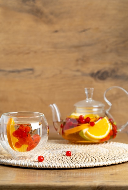 Heller Vitamintee mit Früchten in einer Glasteekanne auf dem Küchentisch auf Holzhintergrund