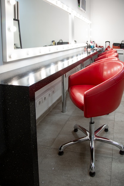 Helles Ankleidezimmer mit roten Stühlen. In einem einfachen Raum zum Schminken stehen mehrere bequeme Stühle hintereinander.