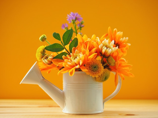 Helles Bouquet von Orangen-Chrysanthemen-Gänseblümchen und violetten Blumen in einer Garten-Gießkanne