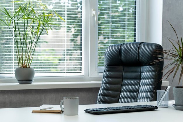 Helles Büro. Komfortabler Arbeitsplatz. Ledersessel. Tastatur, Notizbuch und Tasse Kaffee auf dem Desktop.