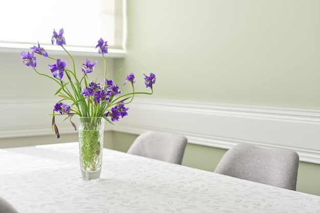 Helles Esszimmerinterieur, Tisch und Stühle in der Nähe des Fensters, Strauß lila Iris in der Vase, weißer Tischdeckenraum, Kopierraum