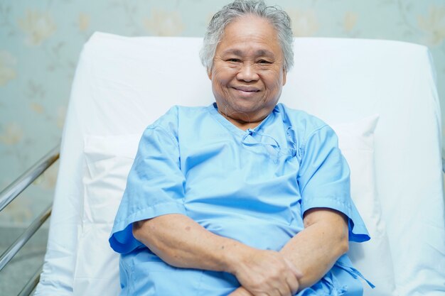 Helles Gesicht des geduldigen Lächelns der asiatischen älteren Frau beim Sitzen auf Bett im Krankenhaus.