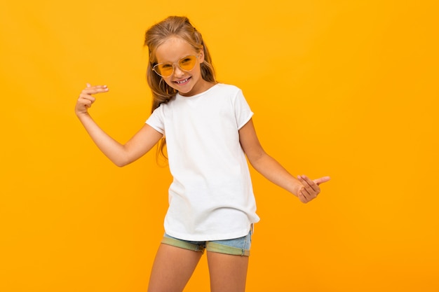 helles Mädchen in der Sonnenbrille in einem weißen T-Shirt auf einer gelben Wand