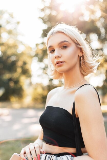 Helles Porträt einer schönen Modefrau mit kurzen Haaren im schwarzen Sommer-Trägershirt geht an einem sonnigen Tag im Park spazieren