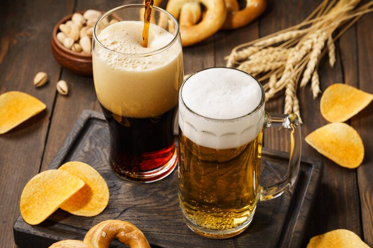 Helles und dunkles Bier mit verschiedenen Snacks - Pommes, Brezeln und Nüssen auf einem dunklen Holztisch.