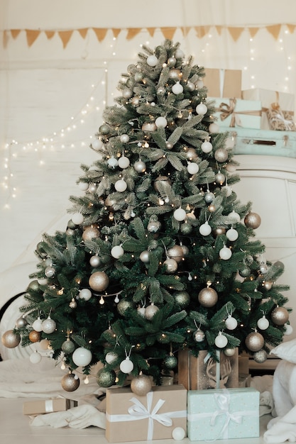 Helles Zimmerinterieur mit geschmücktem Weihnachtsbaum und vielen Geschenkboxen.