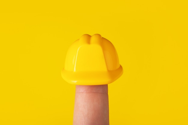 Helm auf Finger über gelbem Hintergrund, Bau-Schutzhelm für Kopf