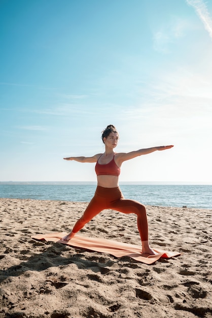 Hembra adulta joven practicando yoga en una playa, pose de Virabhadrasana II, enfoque selectivo