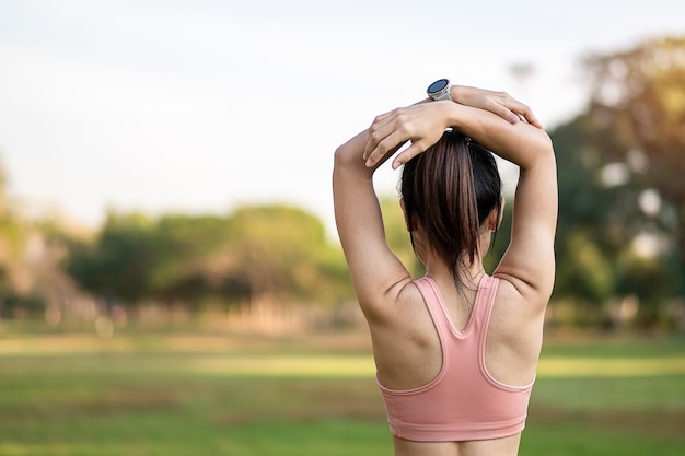 Hembra adulta joven en ropa deportiva rosa estirando los músculos en el parque al aire libre.