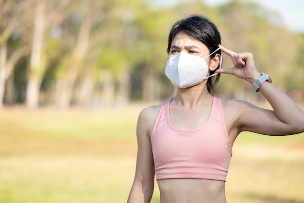 Hembra adulta joven vistiendo N95 mascarilla protectora durante el estiramiento muscular en el parque al aire libre