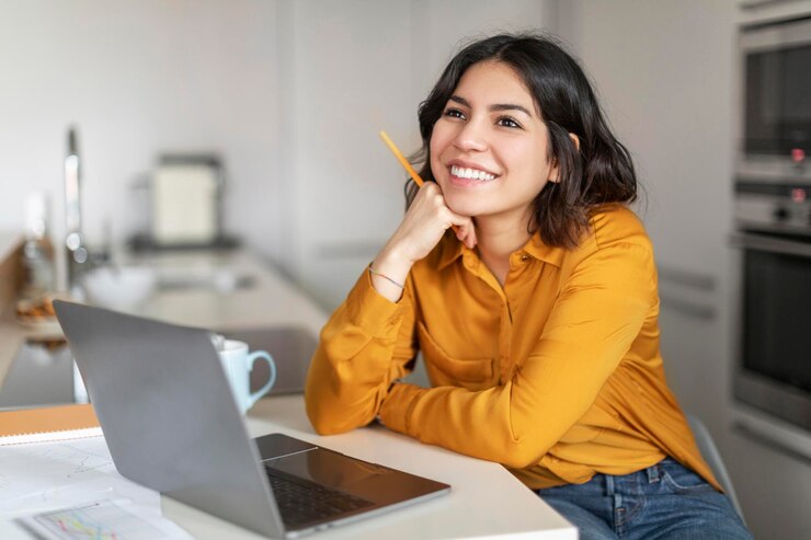 Foto hembra árabe joven soñadora sentada en el escritorio con la computadora portátil en la cocina