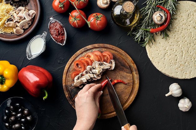 Hembra cortada a mano champiñones y tomates en una tabla de madera en la mesa de la cocina alrededor del ingrediente mentira