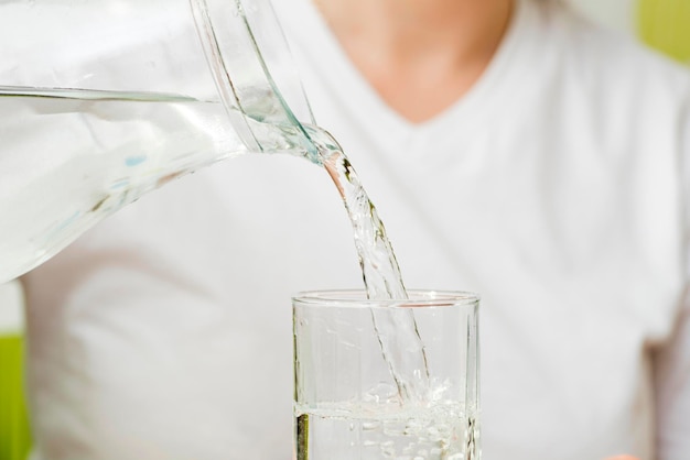 Una hembra está vertiendo agua fresca y clara de una jarra en un vaso