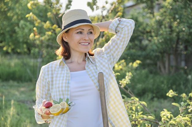 Hembra en jardín en sombrero de paja con plato de fresas menta limón