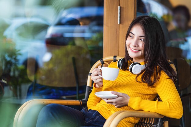 Hembra joven asiática sosteniendo una taza de café y sentada en una moderna cafetería o espacio de coworking