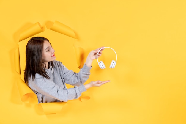 Hembra joven con auriculares sobre papel amarillo rasgado de audio de sonido de ultrasonido de fondo