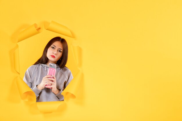 Hembra joven con una botella de agua sobre papel amarillo rasgado de fondo gimnasio atleta interior ajuste